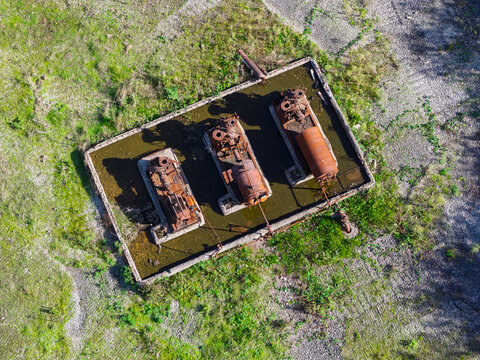 Aerial view of rusted industrial machinery and tanks submerged in a flooded concrete basin at an oil refinery site in the United Kingdom.