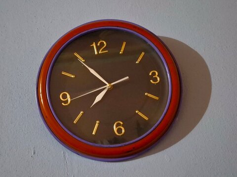 Round wall clock with gold numbers and red frame hanging on blue wall
