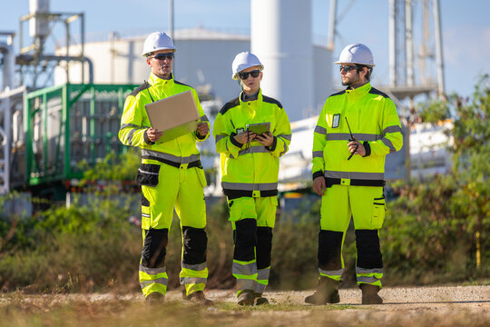 Industrial engineers walking and discussing project with laptop near gas tank plant, Team of industrial inspectors using laptop and tablet while walking at refinery site