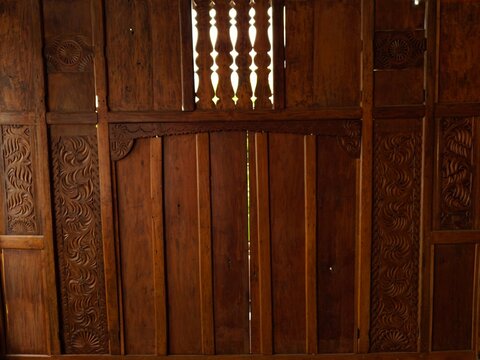 Traditional Javanese wooden house wall and window with detailed ethnic carving, ideal background for Indonesian culture, heritage architecture, and historic interior design.