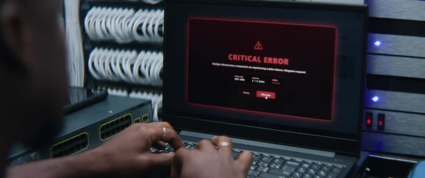 System Administrator Analyzing Live Server Metrics at Workstation in Server Room While Critical System Error Displays on Monitor. IT Incident Response, Network Reliability, and Emergency Diagnostics.