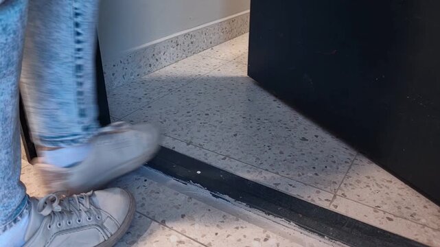 Close-up of a woman's sneakers stepping over a doorway threshold toward the stairs in a modern apartment building, leaving the floor, daily movement, urban routine.
