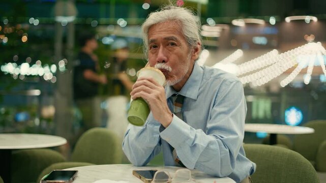 Relaxed senior businessman drinks matcha looking aside by cafe window