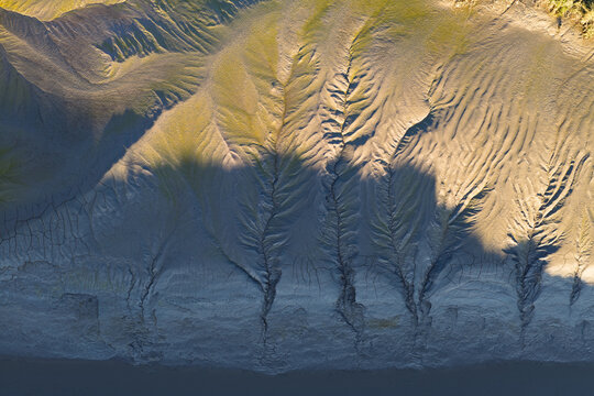 Aerial view of intricate erosion patterns and tidal channels carved into the mudflats of an estuary, with soft golden light highlighting the textures of the silt and clay, United Kingdom.