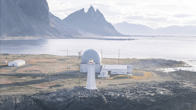 Aerial view of the Vestrahorn lighthouse and radar station situated on a rocky coastline with dramatic mountains in the background in Iceland.