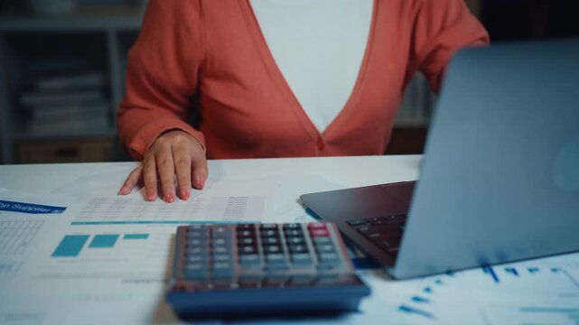Close up young Asian woman calculates bills and household expenses with calculator and laptop at home at night. Personal finance budgeting, tax payment plan, debt control, savings mortgage management.
