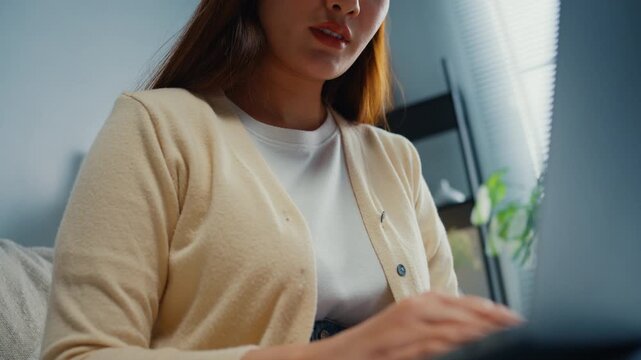 Close up young Asian woman reviews financial documents, bills and expenses on laptop at home. Personal finance budget planning, Tax invoice paperwork review, Household savings and expense management.