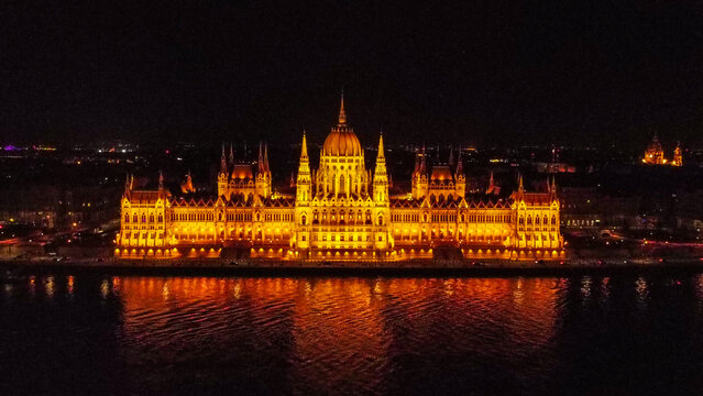 Aerial view of the illuminated Hungarian Parliament Building at night, reflecting on the dark waters of the Danube River in Budapest, Hungary.
