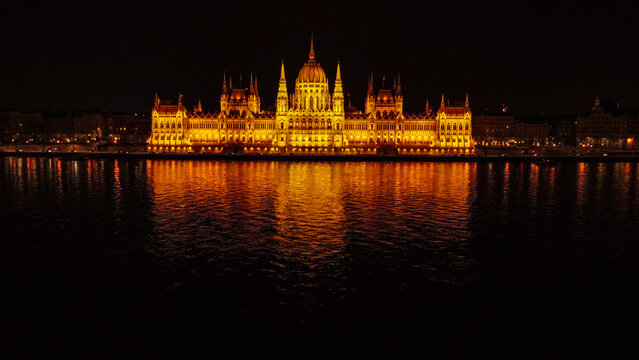Aerial view of Hungarian Parliament Building illuminated at night with golden lights reflecting on the dark waters of the Danube River, Budapest, Hungary.