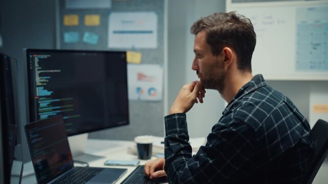 Young Caucasian male programmer writes code using multiple screens in home office workspace. AI development, cybersecurity, network database system, software engineering, remote tech startup concept.