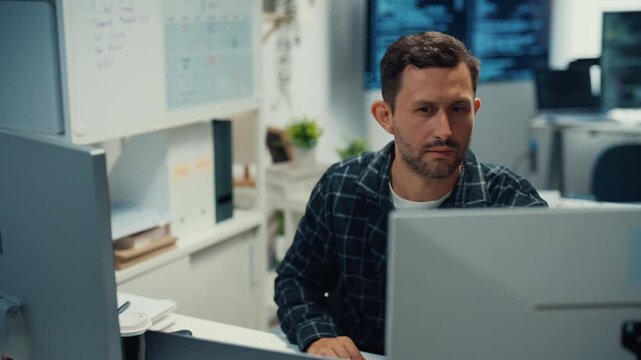 Young Caucasian male programmer writes code using multiple screens in home office workspace. AI development, cybersecurity, network database system, software engineering, remote tech startup concept.