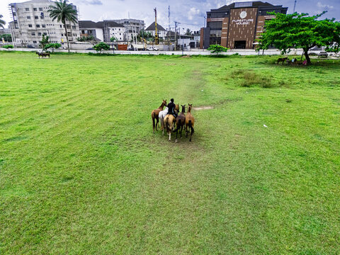 Aerial view of riders on horseback at the Port Harcourt Polo Club, with lush green grass, surrounding urban buildings, and a clear sky in Port Harcourt, Rivers, Nigeria.