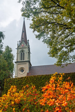 Church steeple rising above autumn garden foliage in Switzerland countryside