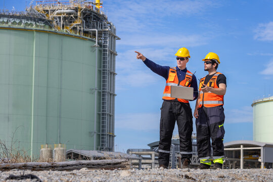 Industrial engineers holding laptop and walkie talkie during site inspection at refinery plant, Two male technicians in hard hats inspecting chemical plant facility outdoors