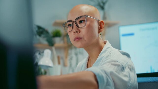 Young Asian businesswoman types on keyboard at computer workstation in modern office. Focused employee, business productivity, digital workflow, data review and financial analysis concept.