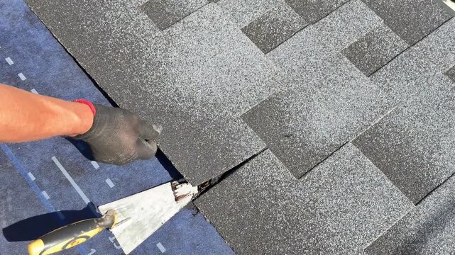 Worker aligns bitumen roof shingles with adhesive, roofing installation