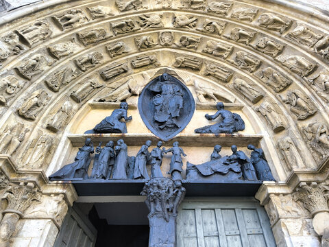Gothic cathedral tympanum with bronze sculptures and carved stone archivolts above old wooden doors