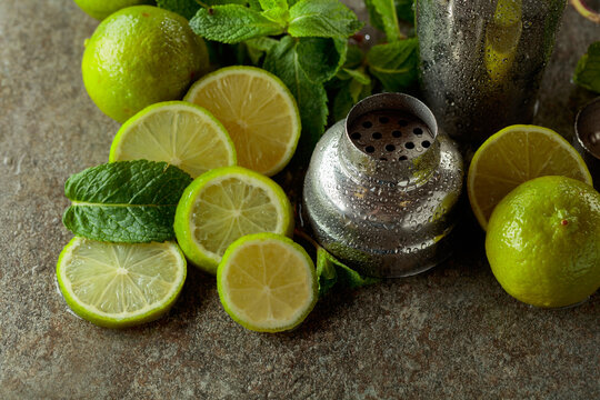 Shaker, limes, and  fresh mint branches on a stone table.