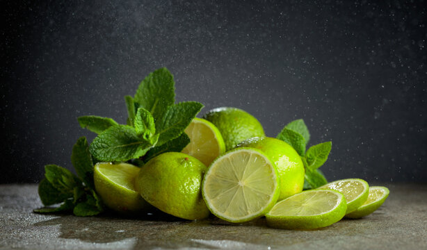 Lime slices and fresh mint branches on a stone table.