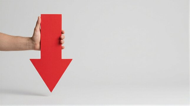 Hand holding large red downward arrow against plain white background. Pointing down gesture with copy space on right. Decline, loss and decrease concept. Warning, crisis and market drop