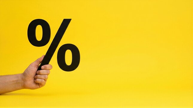 Hand holding black percent sign on bright yellow background with copy space. Percent symbol close-up. Discount, sale and price reduction concept. Interest rate and finance. Promotion, offer.