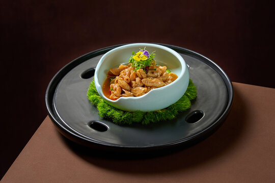 Braised fish maw in brown sauce served in pale blue bowl on dark slate round plate, 45-degree angle, dark brown backdrop