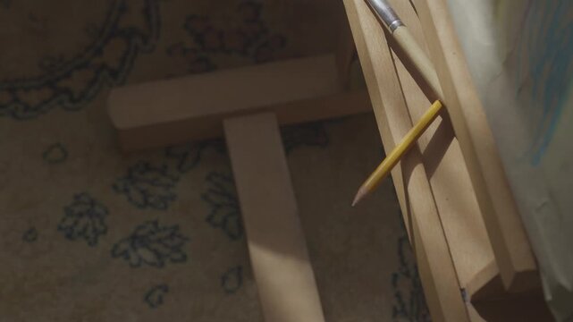A slow pan reveals paintbrushes arranged on an easel tray in an ambient-lit studio during a creative painting hobby session.