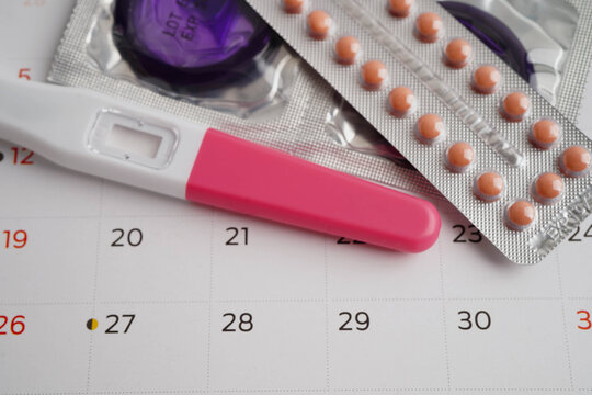 Pregnancy test with birth control pills and condom for female on calendar, ovulation day.