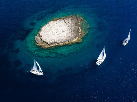 Aerial view of sailing yachts cruising around Taljuric rocky islet in Telascica Nature Park, Croatia