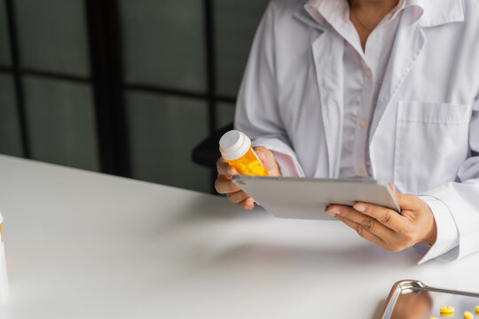 Mature Asian pharmacist using tablet and holdng medicine bottle