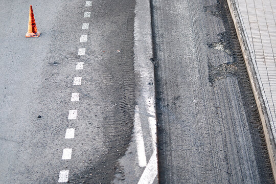 Road repair, asphalt repaving construction site, milled pavement, white lane markings. Road repair work. Scraped asphalt street surface prepared for resurfacing with safety orange traffic cone