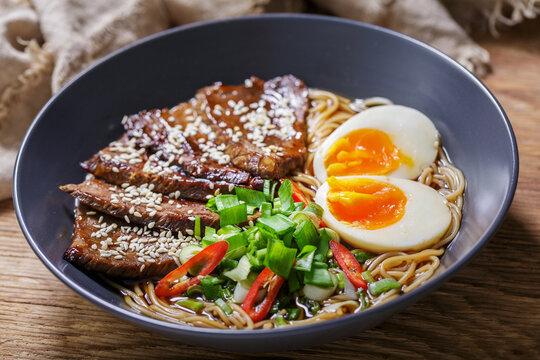 Ramen soup with beef, egg and chives on wooden table
