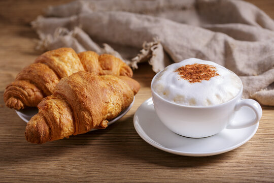 cup of cappuccino coffee with croissantc on wooden table