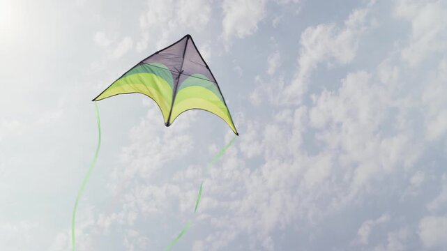Green and yellow kite with long ribbon tails against a cloudy sky slow motion close-up shot from the bottom up