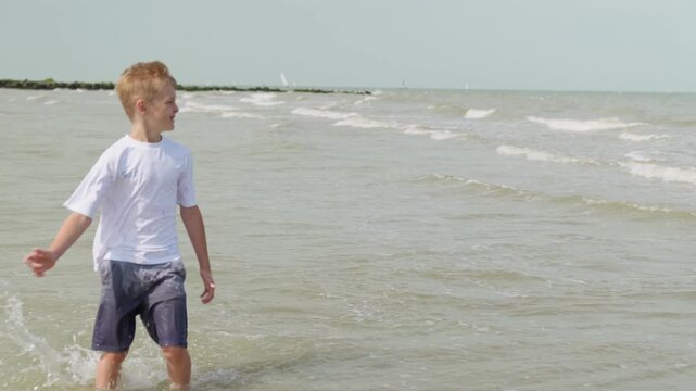 A boy runs away from the waves at the beach kneeling in the water