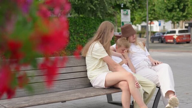 Woman and two children sitting together on a wooden bench in town family time in the city