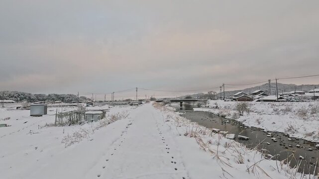 雪の積もった川沿いの道を歩く
