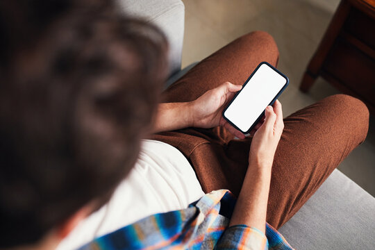 Young man using smartphone with blank screen on sofa at home - mockup