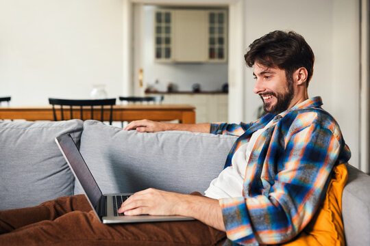 Smiling man using laptop on sofa in living room at home