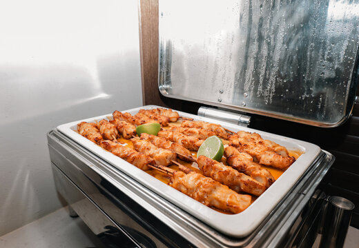 Grilled chicken skewers with lime slices in a buffet chafing dish