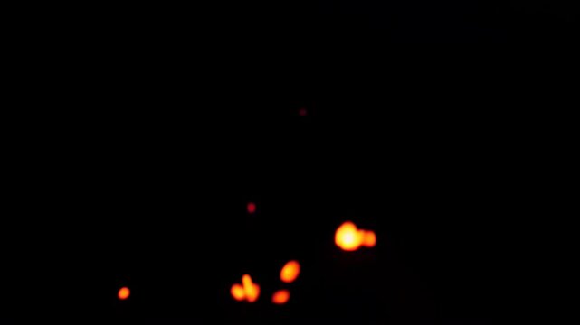 Glowing orange sparks rise and scatter through dark air, creating a dramatic abstract fire particle display with bright embers and atmospheric motion