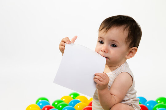Baby chewing white paper with colorful plastic balls