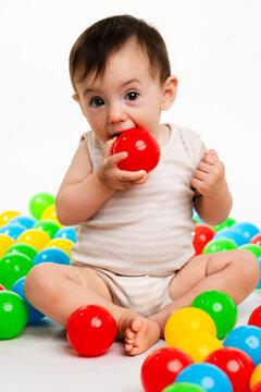 Baby chewing red toy ball playing with colorful pit