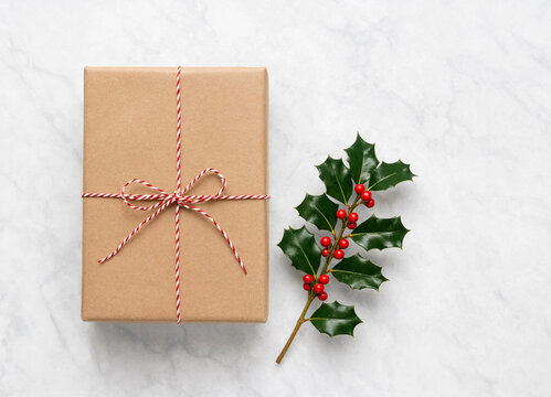 Wrapped brown paper present box decorated with red and white string and a holly branch with berries