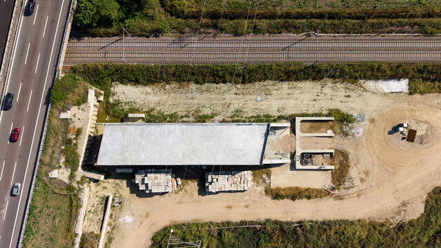 Aerial view of the construction site for a railway tunnel featuring concrete structures, stacks of building materials, and adjacent highway lanes in Milan, Lombardy, Italy.