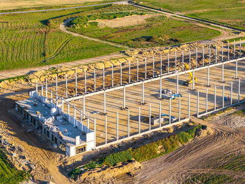 Aerial view of a construction site featuring a steel framework with concrete pillars, construction machinery, and heavy equipment in an open field in Kwidzyn, Pomeranian Voivodeship, Poland.