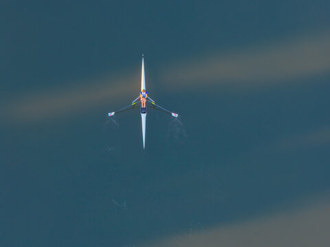 Aerial view of a lone rower in a scull boat gliding across calm dark water, creating subtle ripples in Gdansk, Pomeranian Voivodeship, Poland.