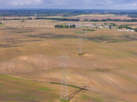 Aerial view of high-voltage power lines stretching across vast agricultural fields under a cloudy sky in Pelplin, Pomeranian Voivodeship, Poland.