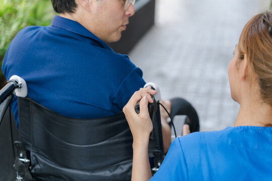 Over the shoulder view of nurse holding wheelchair handle and talking to senior patient.