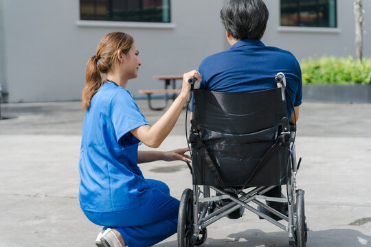 Rear view of female nurse talking to senior male patient in a wheelchair outdoor.